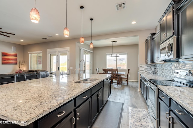 kitchen featuring open floor plan, visible vents, stainless steel appliances, a large island with sink, and a sink