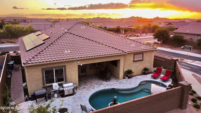 rear view of property featuring solar panels, a tile roof, a patio, stucco siding, and an outdoor pool