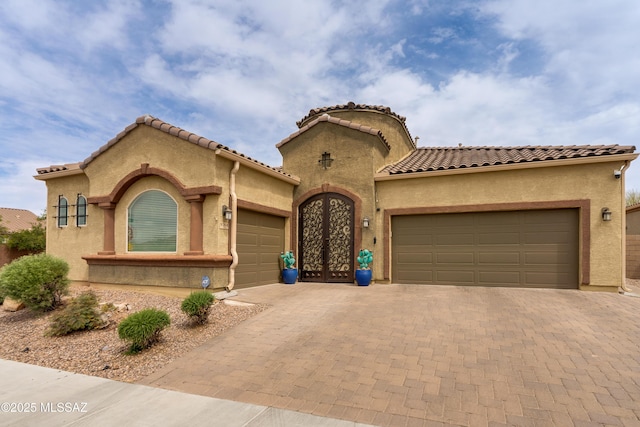 mediterranean / spanish home with an attached garage, french doors, stucco siding, and decorative driveway