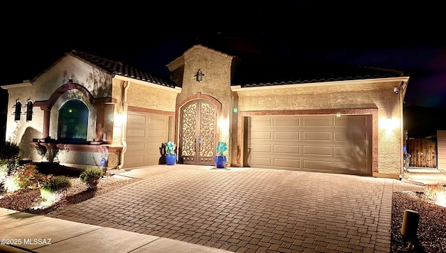 mediterranean / spanish-style home with an attached garage, a tile roof, stucco siding, french doors, and decorative driveway