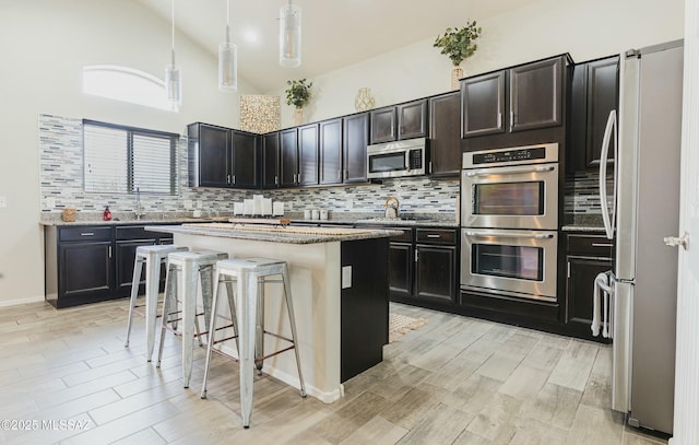 8754 W Denstone Rd, Marana, AZ 85653 - kitchen featuring appliances with stainless steel finishes, decorative backsplash, a kitchen breakfast bar, light stone countertops, and high vaulted ceiling