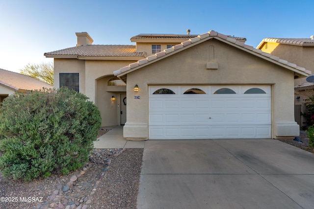 mediterranean / spanish house with driveway, a tiled roof, an attached garage, a chimney, and stucco siding
