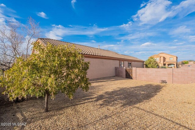 back of property with stucco siding, a tile roof, fence, and a gate