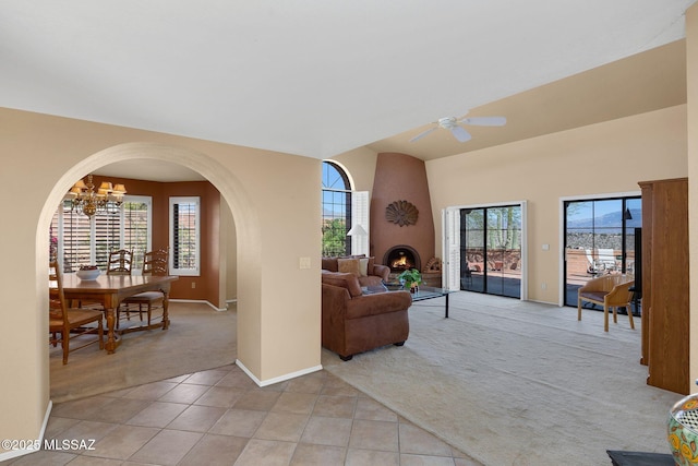 living area featuring arched walkways, light colored carpet, light tile patterned floors, ceiling fan with notable chandelier, and baseboards