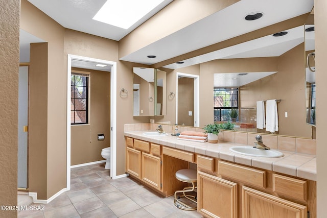 full bath featuring toilet, double vanity, a sink, and baseboards