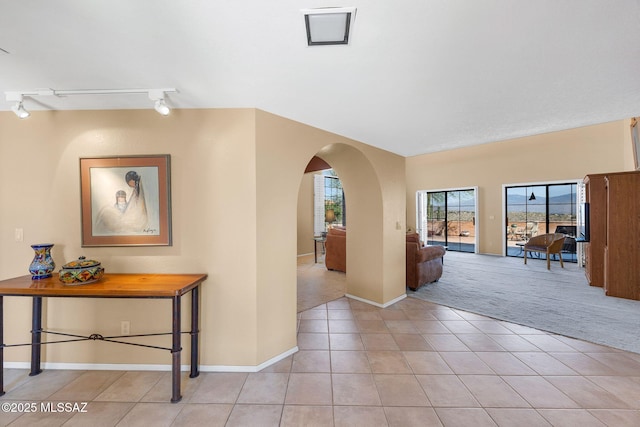 hallway featuring light tile patterned flooring, rail lighting, light carpet, baseboards, and arched walkways