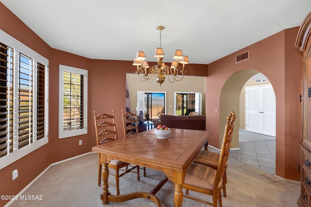 dining room with arched walkways, a healthy amount of sunlight, light colored carpet, a chandelier, and visible vents