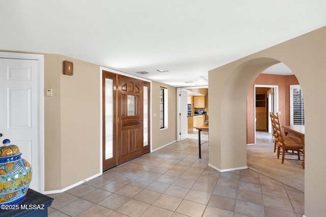 entrance foyer with baseboards, visible vents, arched walkways, and light tile patterned flooring