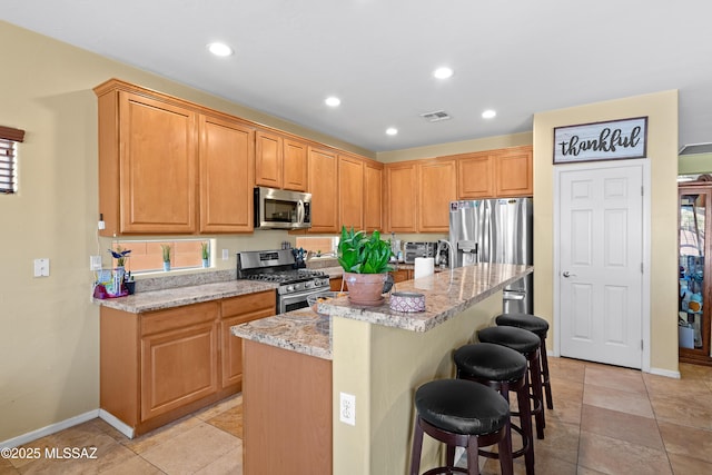 kitchen with visible vents, stainless steel appliances, a kitchen island, light stone counters, and a breakfast bar area
