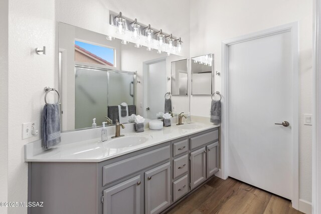 full bath with double vanity, a sink, a shower stall, and wood finished floors