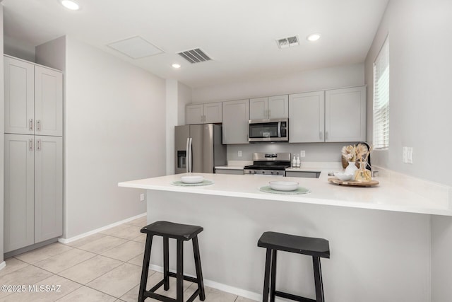 kitchen featuring a peninsula, visible vents, light countertops, stainless steel appliances, and a breakfast bar area