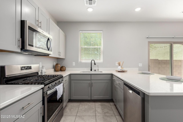 kitchen featuring visible vents, a sink, a peninsula, gray cabinetry, and stainless steel appliances