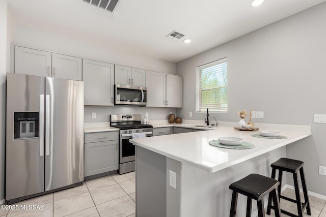 kitchen with a peninsula, appliances with stainless steel finishes, a sink, and visible vents