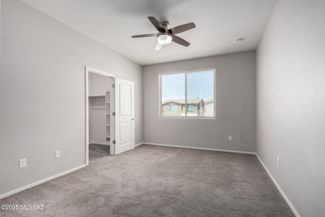 unfurnished bedroom with a walk in closet, carpet floors, a closet, baseboards, and ceiling fan