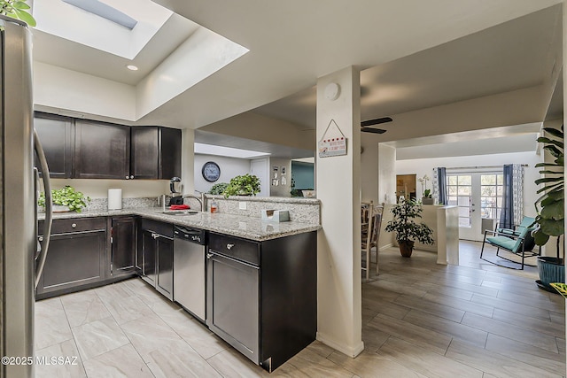 kitchen with light stone counters, a sink, a skylight, stainless steel appliances, and dark brown cabinets