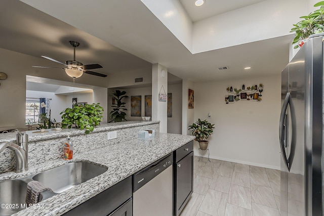 kitchen with a sink, light stone countertops, appliances with stainless steel finishes, baseboards, and ceiling fan