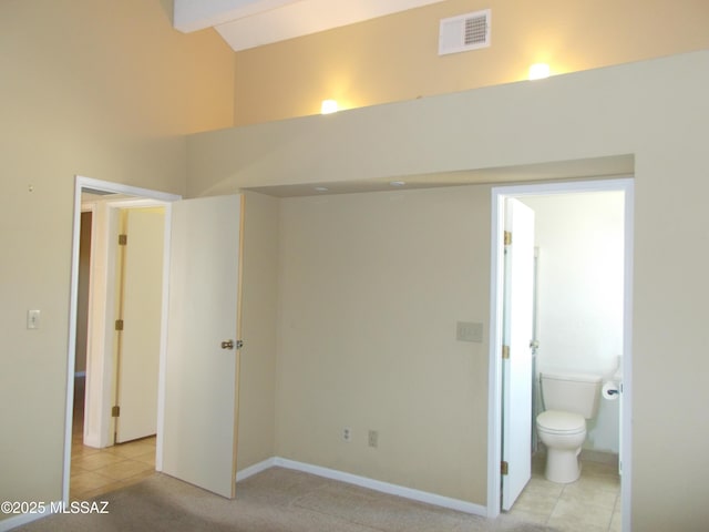 unfurnished bedroom with a high ceiling, visible vents, light tile patterned floors, ensuite bath, and baseboards