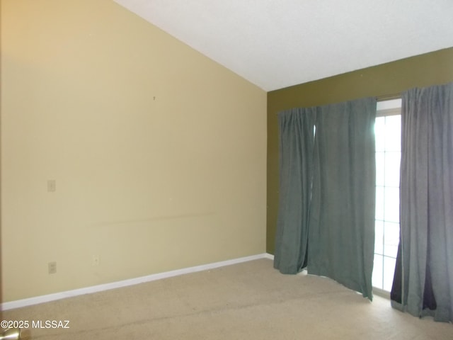 spare room with light carpet, vaulted ceiling, and baseboards