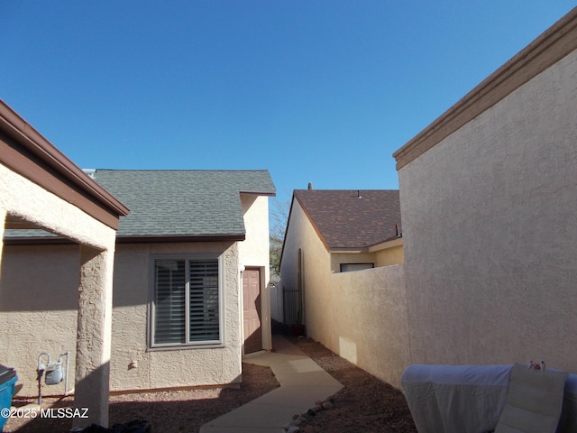view of home's exterior featuring roof with shingles, stucco siding, and fence