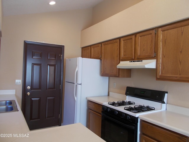 kitchen featuring brown cabinetry, under cabinet range hood, gas stove, and freestanding refrigerator