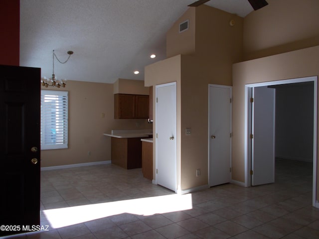 kitchen with high vaulted ceiling, brown cabinets, light tile patterned flooring, and a notable chandelier