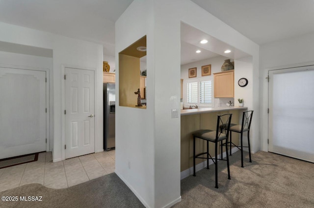 kitchen with light brown cabinets, stainless steel fridge with ice dispenser, a breakfast bar area, and light carpet