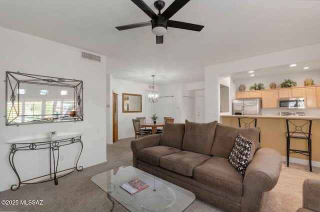 living room featuring ceiling fan with notable chandelier, visible vents, and light colored carpet
