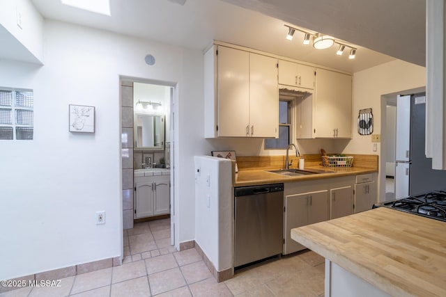 kitchen with light countertops, light tile patterned floors, stainless steel dishwasher, a sink, and freestanding refrigerator