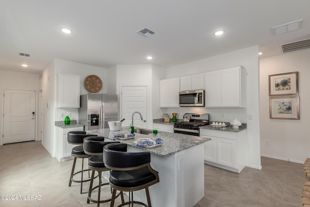 kitchen with a breakfast bar, appliances with stainless steel finishes, an island with sink, a sink, and light stone counters