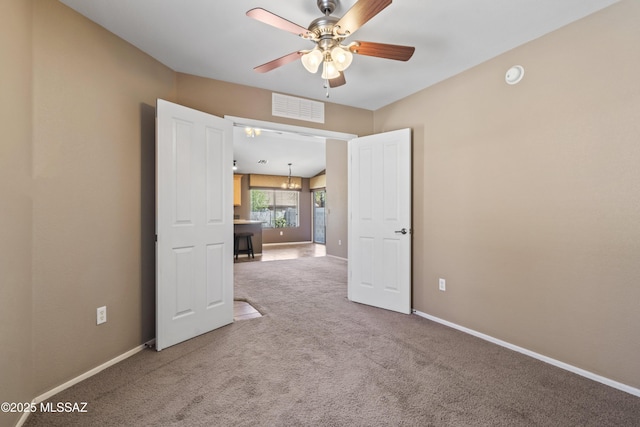 carpeted empty room featuring ceiling fan with notable chandelier, visible vents, and baseboards