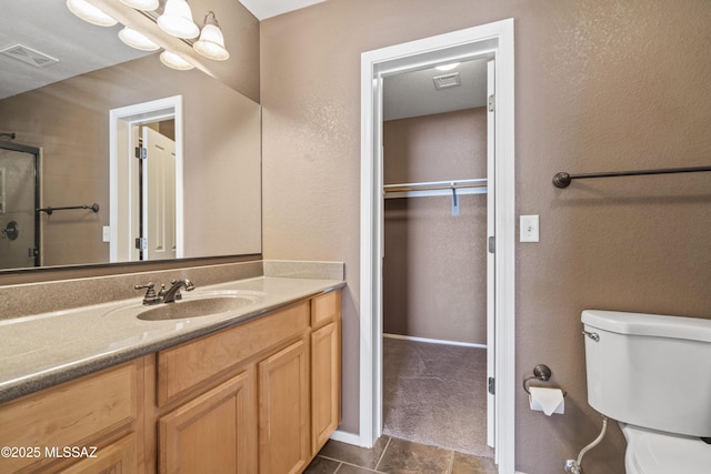 bathroom featuring a shower with door, visible vents, toilet, and vanity