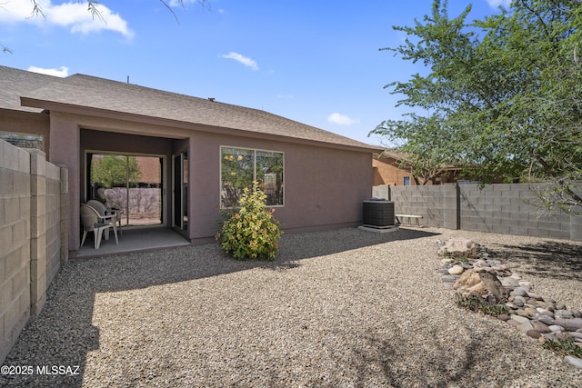 rear view of house with stucco siding, central AC unit, fence private yard, and a patio area