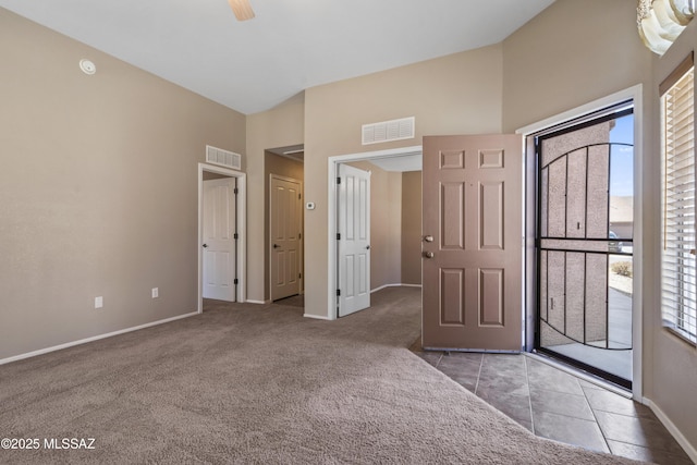 carpeted foyer entrance with tile patterned floors, high vaulted ceiling, baseboards, and visible vents
