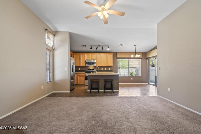 kitchen featuring appliances with stainless steel finishes, open floor plan, dark colored carpet, a kitchen island with sink, and baseboards