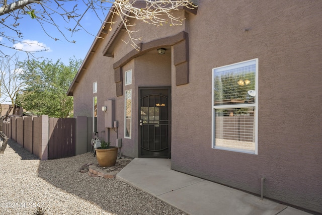 view of exterior entry with stucco siding and fence