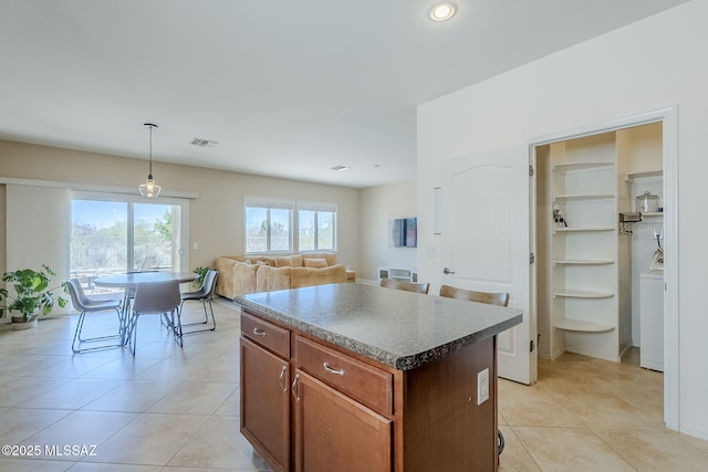 kitchen with light tile patterned floors, a center island, washer / dryer, and decorative light fixtures