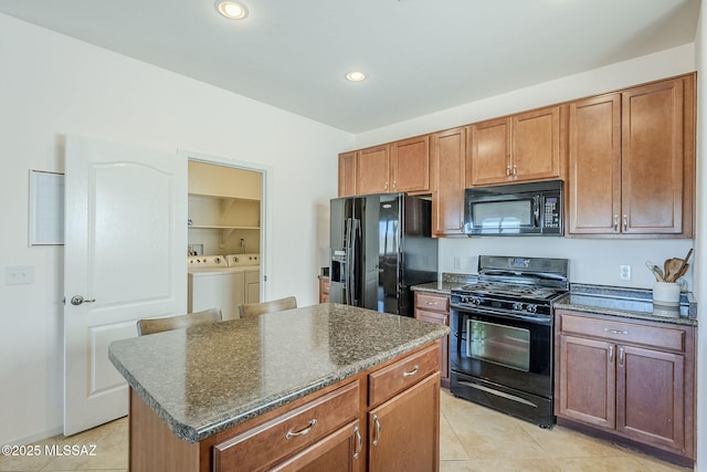 kitchen featuring brown cabinetry, a center island, light tile patterned floors, black appliances, and washer and clothes dryer