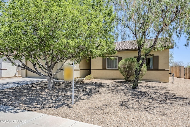 view of front of house featuring fence, a tiled roof, and stucco siding