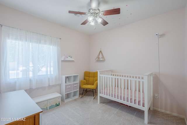 carpeted bedroom featuring a ceiling fan and a crib