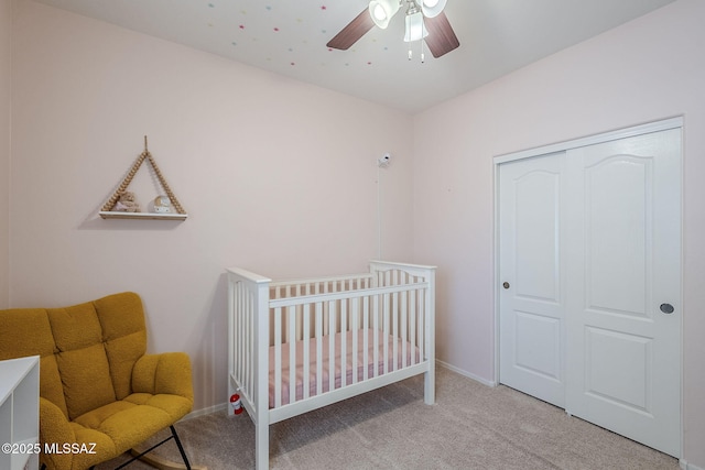 bedroom featuring ceiling fan, a nursery area, baseboards, a closet, and carpet flooring