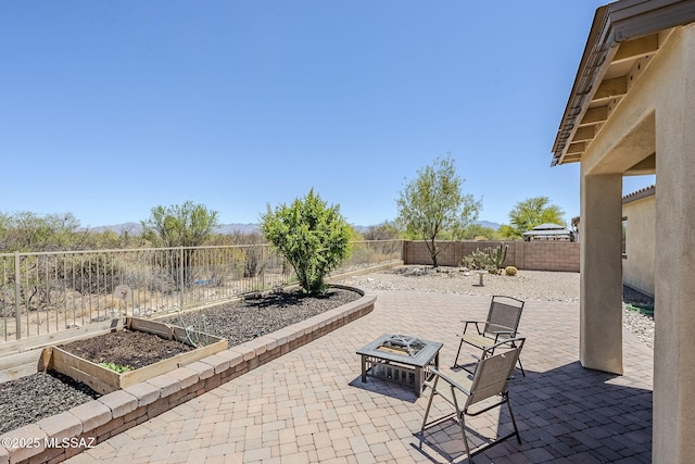 view of patio / terrace featuring a fenced backyard, a fire pit, a mountain view, and a vegetable garden
