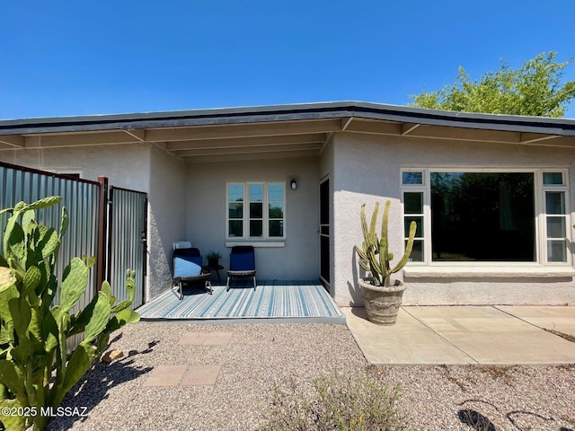 rear view of house featuring a patio, stucco siding, and fence