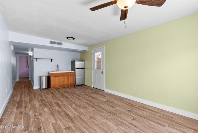 kitchen with freestanding refrigerator, a ceiling fan, light wood-style floors, visible vents, and a sink
