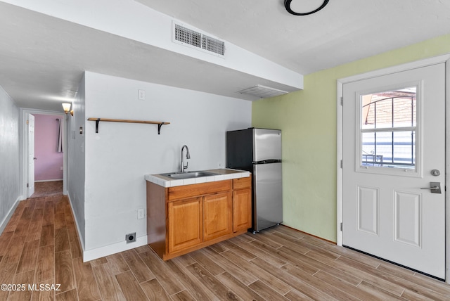 kitchen featuring visible vents, a sink, freestanding refrigerator, tile counters, and wood finish floors
