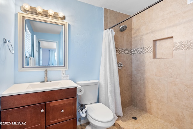 bathroom with toilet, a tile shower, and vanity
