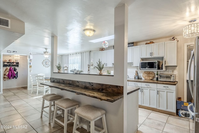 kitchen featuring decorative backsplash, white cabinets, appliances with stainless steel finishes, a breakfast bar area, and light tile patterned floors