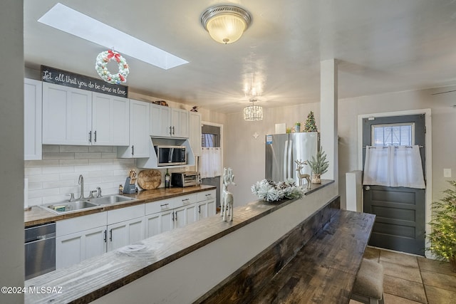 kitchen with a sink, tasteful backsplash, a skylight, butcher block counters, and stainless steel appliances