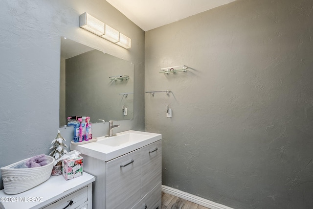 bathroom with a textured wall, baseboards, wood finished floors, and vanity