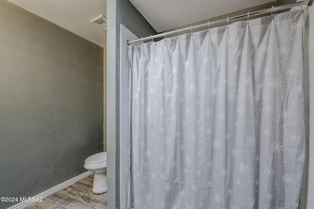 bathroom featuring a shower with shower curtain, toilet, wood finished floors, baseboards, and visible vents