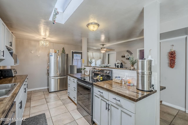 kitchen with a skylight, appliances with stainless steel finishes, butcher block counters, light tile patterned floors, and white cabinets